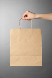 Woman holding kraft paper bag on grey background, closeup. Mockup for design