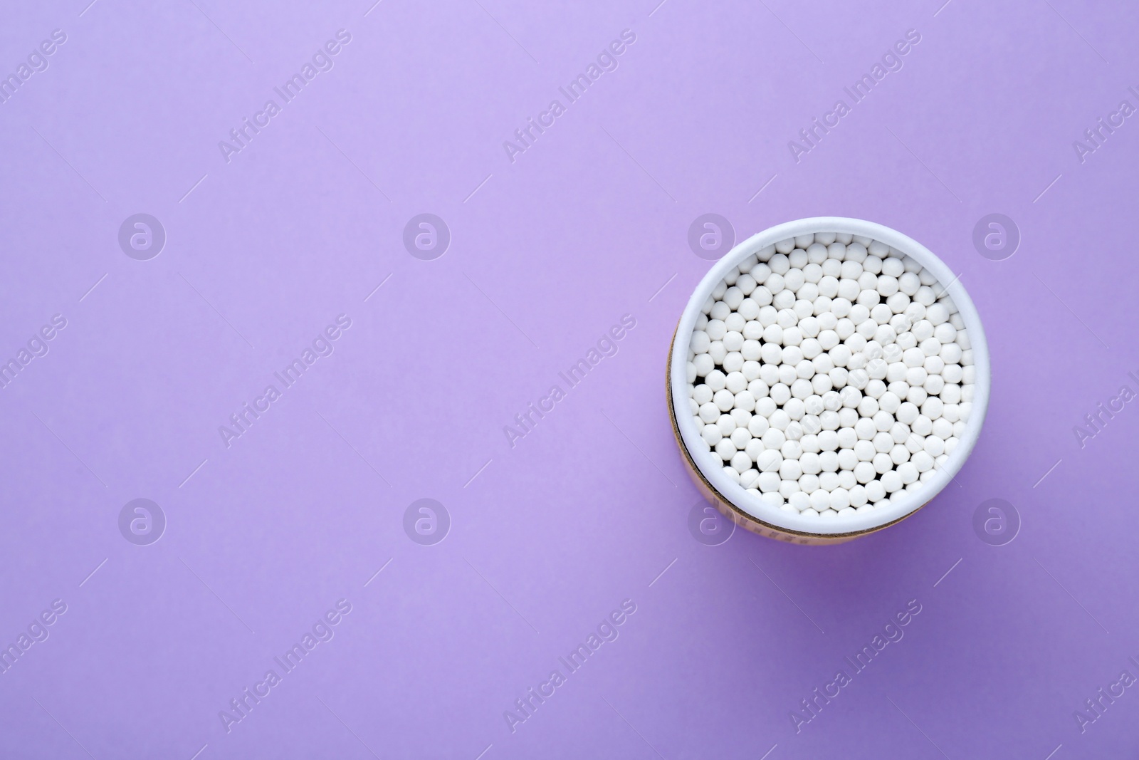 Photo of Container with new cotton buds on violet background, top view. Space for text