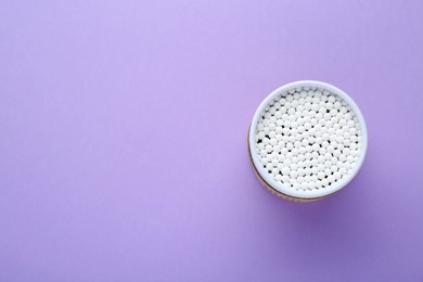 Container with new cotton buds on violet background, top view. Space for text