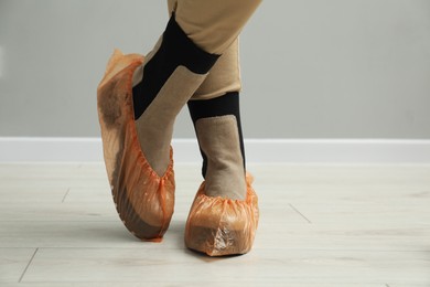 Photo of Woman wearing bright shoe covers onto her boots indoors, closeup