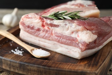 Photo of Pieces of raw pork belly, salt and rosemary on wooden table, closeup