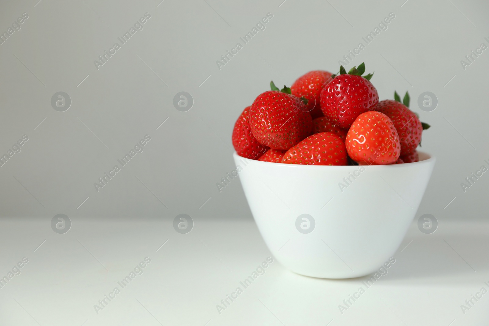 Photo of Fresh juicy strawberries in bowl on white table, space for text