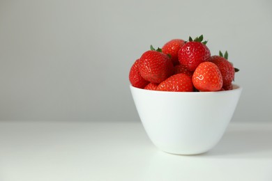 Fresh juicy strawberries in bowl on white table, space for text