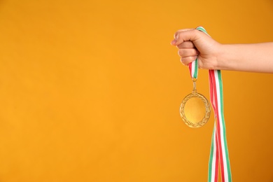 Photo of Woman holding gold medal on yellow background, closeup. Space for text