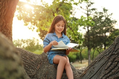 Cute little girl reading book on tree in park