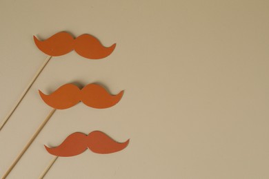 Fake paper mustaches party props on beige background, flat lay. Space for text
