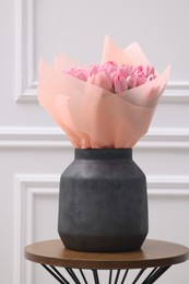 Bouquet of beautiful pink tulips in vase on wooden table near white wall