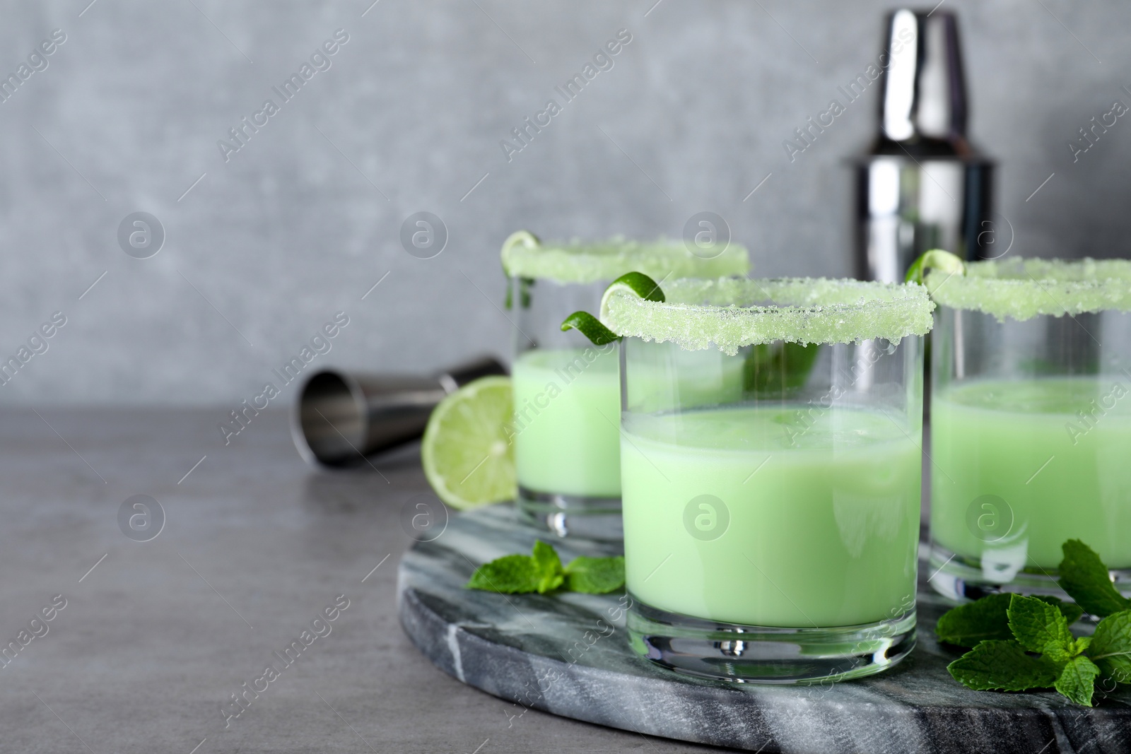 Photo of Delicious mint liqueur with ice cubes and green leaves on grey table. Space for text