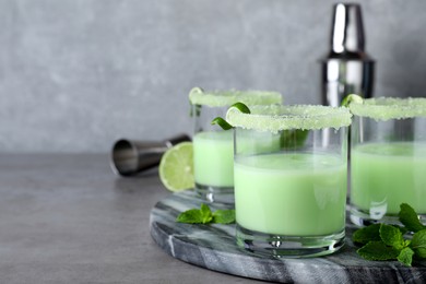 Photo of Delicious mint liqueur with ice cubes and green leaves on grey table. Space for text