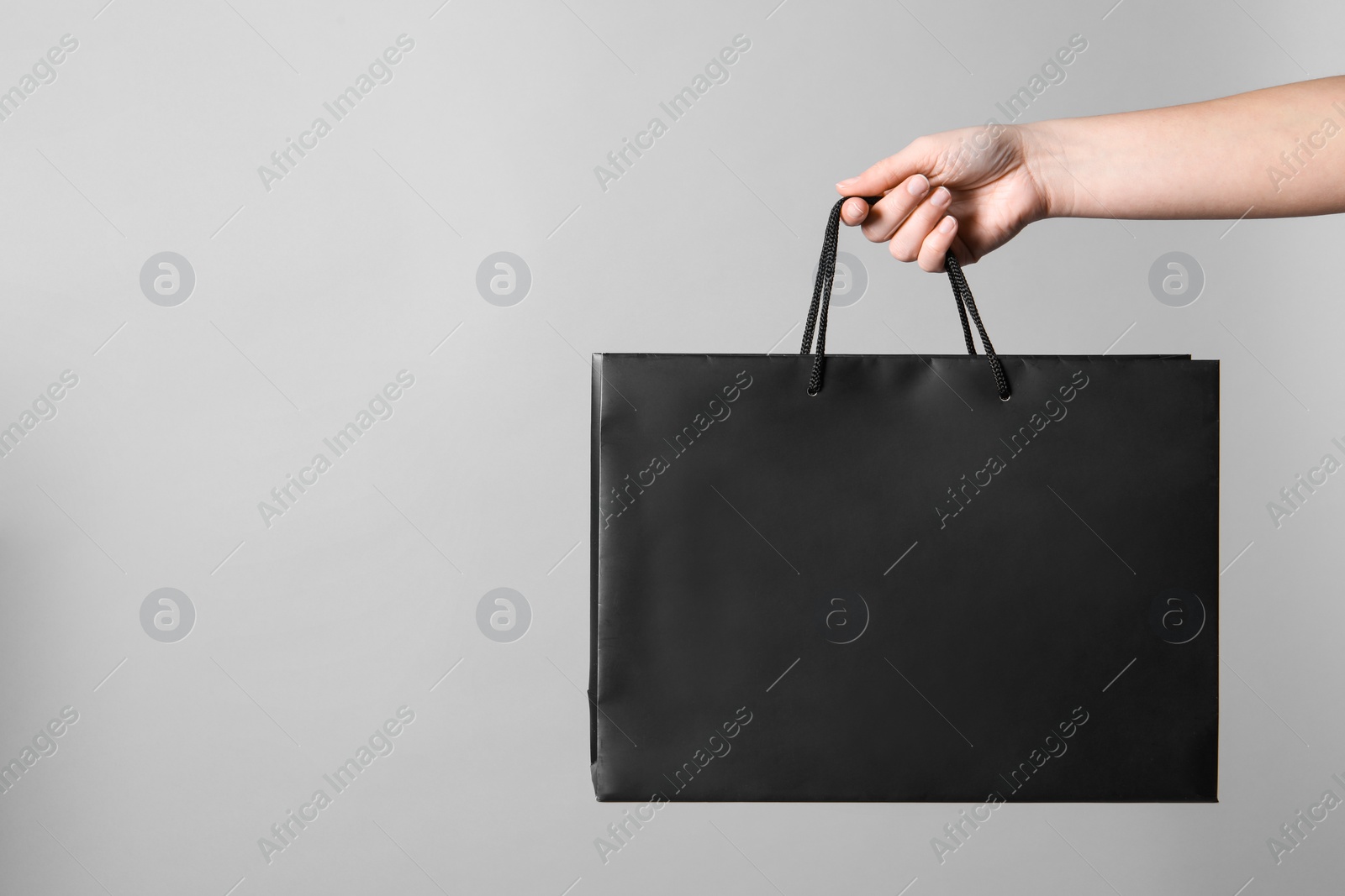 Photo of Woman holding paper shopping bag on grey background, closeup. Space for text