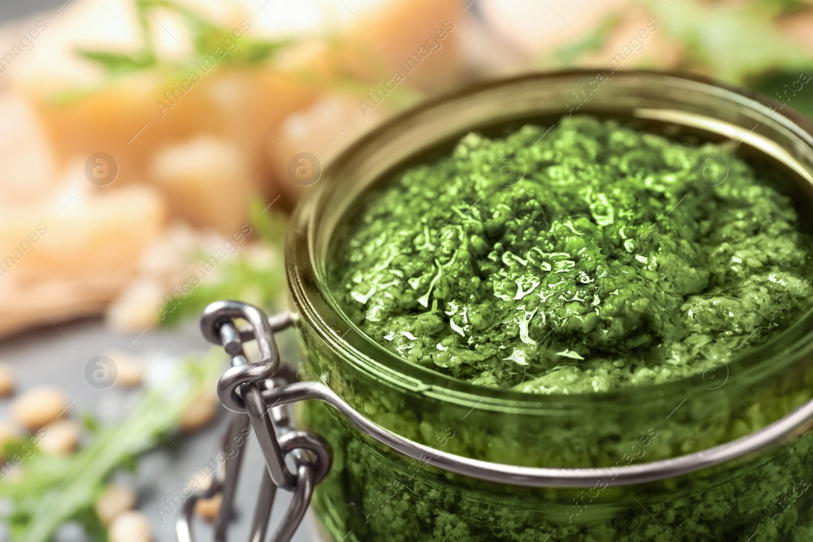 Photo of Jar of tasty arugula pesto on table, closeup