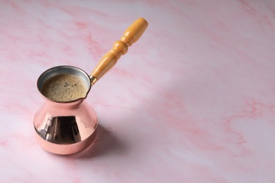 Photo of Turkish coffee in cezve on pink marble table. Space for text