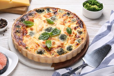 Delicious homemade quiche, ingredients and spatula on table