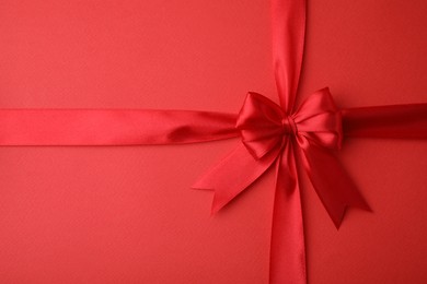 Photo of Bright satin ribbon with bow on red background, top view