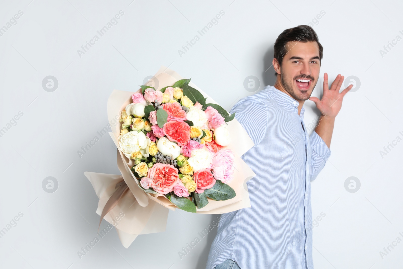 Photo of Young handsome man with beautiful flower bouquet on light background