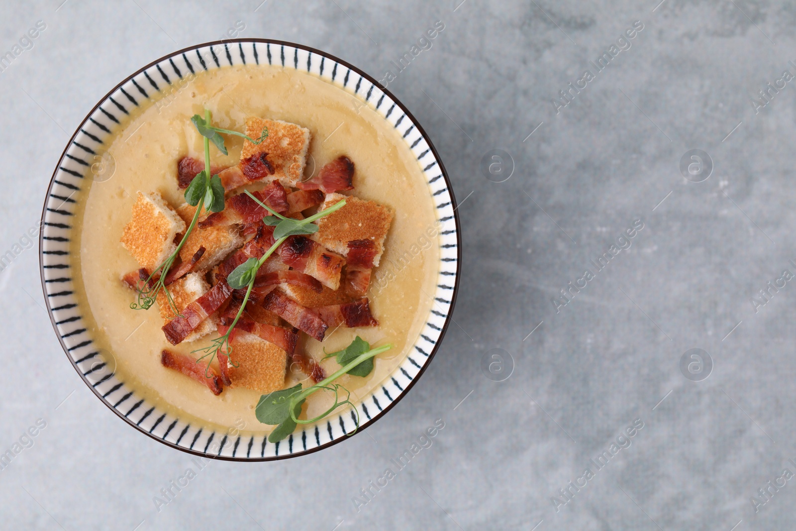 Photo of Delicious lentil soup with bacon and microgreens in bowl on gray table, top view. Space for text