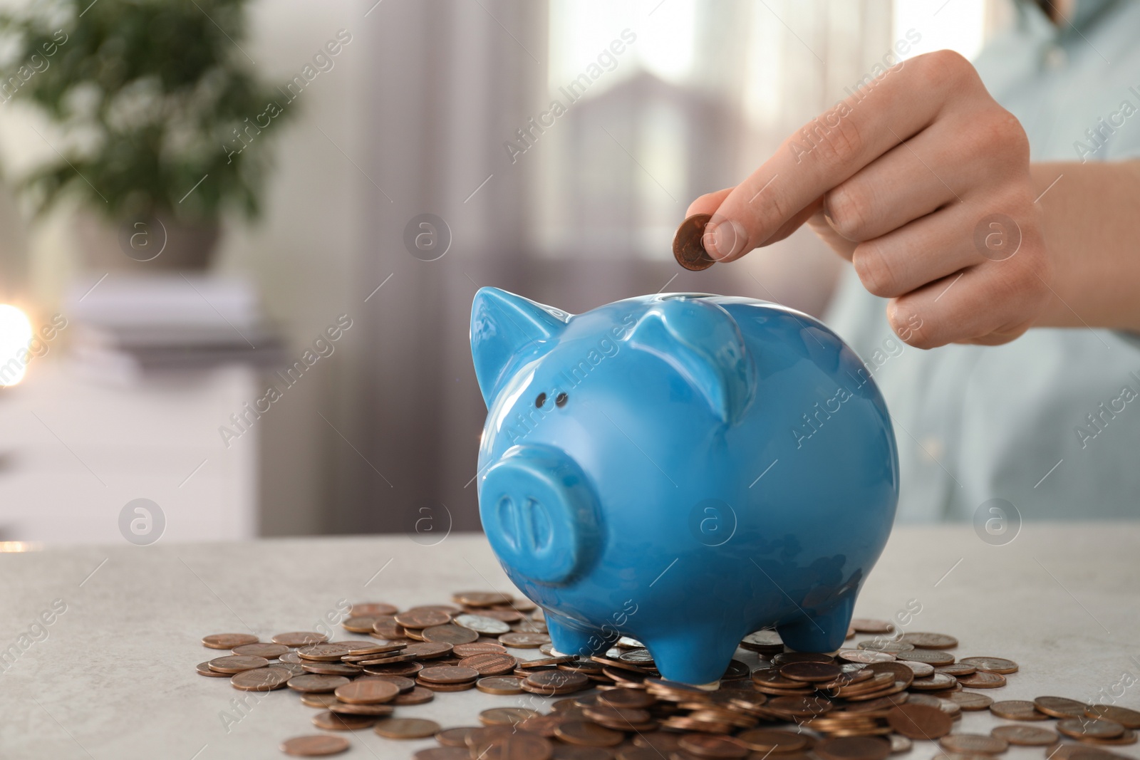 Photo of Man putting coin into piggy bank at table indoors, closeup