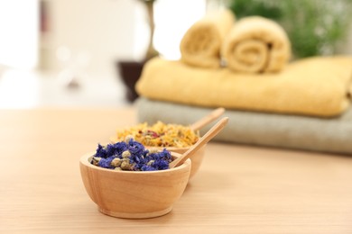 Photo of Bowls with dry flowers and spoons on light wooden table, space for text. Spa therapy