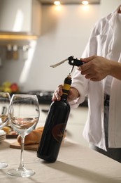 Woman opening wine bottle with corkscrew at table indoors, closeup