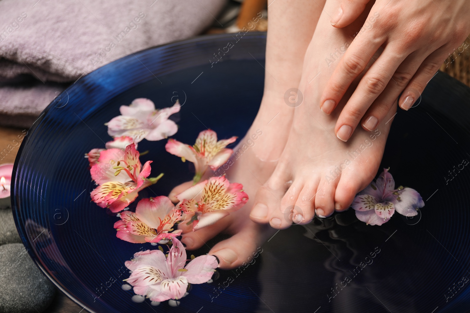 Photo of Woman soaking her feet in bowl with water and flowers, closeup. Spa treatment