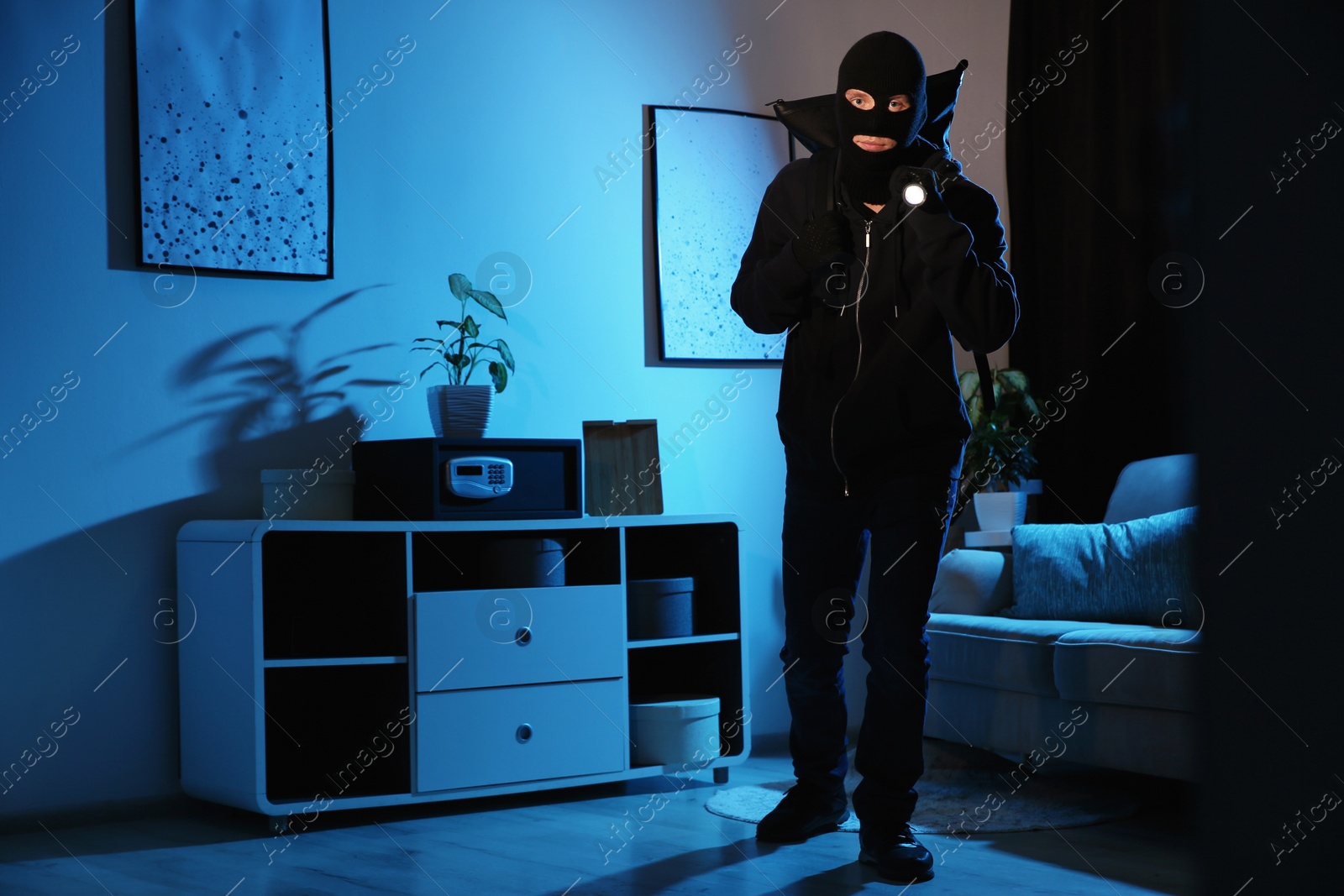 Photo of Thief with flashlight near steel safe indoors at night