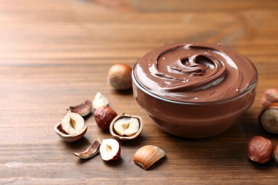 Glass bowl with tasty chocolate hazelnut spread and nuts on wooden table. Space for text