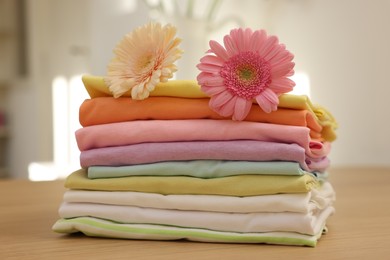 Photo of Stack of clean clothes and flowers on wooden table