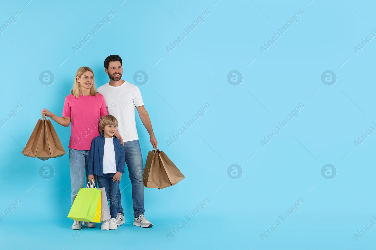 Photo of Happy family with shopping bags on light blue background. Space for text