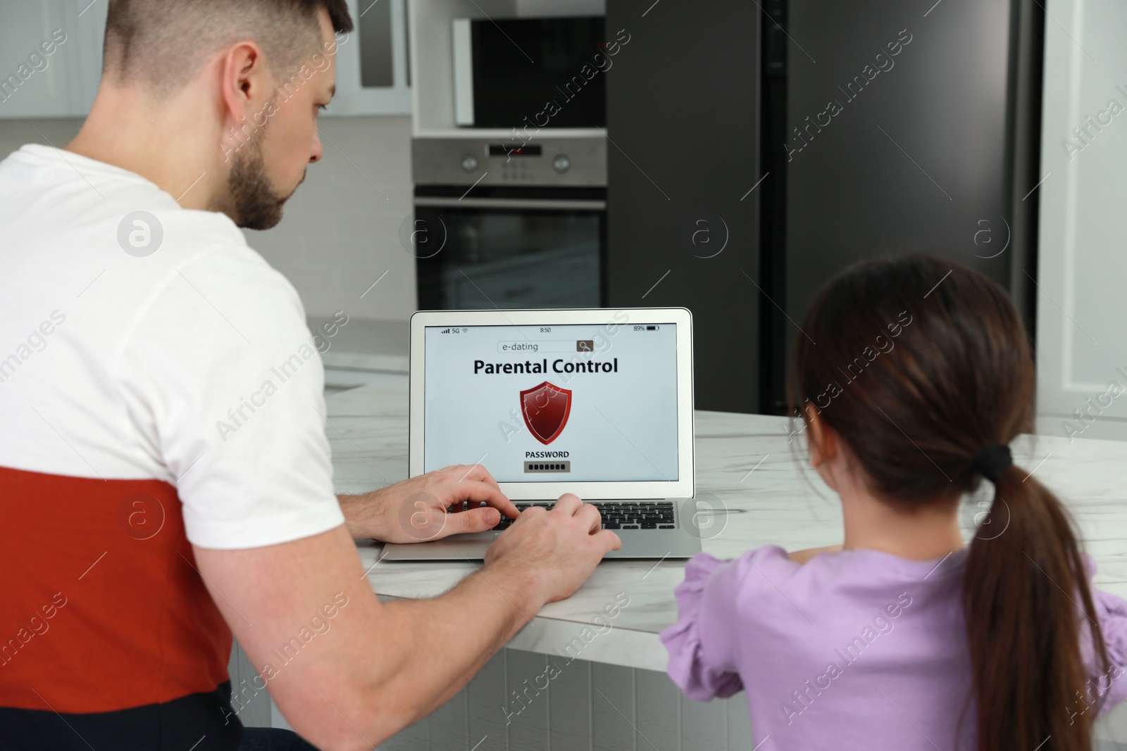 Photo of Dad installing parental control on laptop at table in kitchen, back view. Child safety