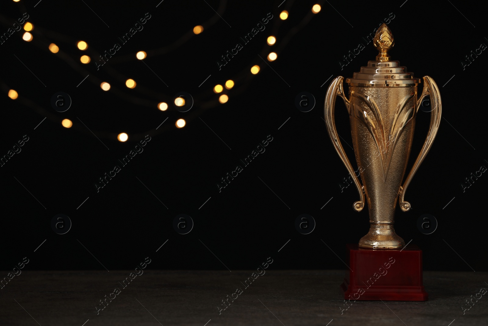 Photo of Golden trophy cup on table against blurred festive lights, space for text