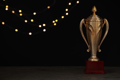 Photo of Golden trophy cup on table against blurred festive lights, space for text