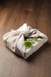 Photo of Furoshiki technique. Gift packed in white fabric decorated with beautiful flowers on wooden table