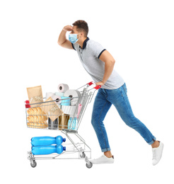 Image of Young man in medical mask and shopping cart with purchases on white background. Coronavirus pandemic 