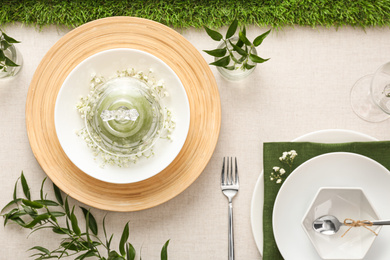 Elegant table setting with green plants on light cloth, flat lay