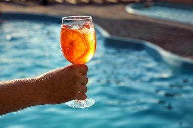 Photo of Man with glass of fresh summer cocktail near swimming pool outdoors, closeup. Space for text