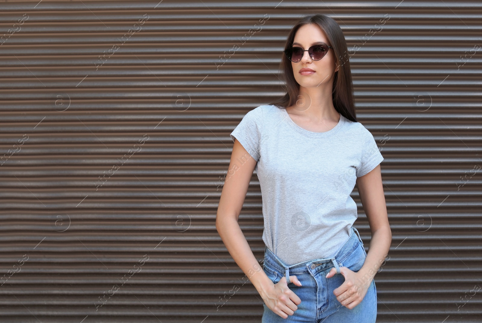 Photo of Young woman wearing gray t-shirt near wall on street. Urban style