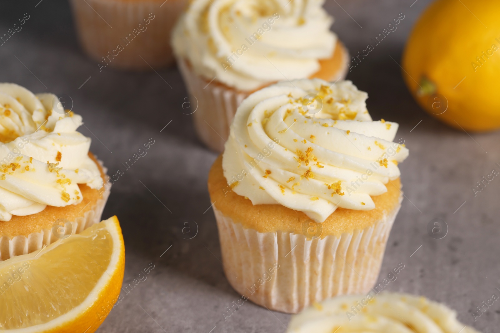 Photo of Delicious cupcakes with white cream and lemon zest on gray table, closeup