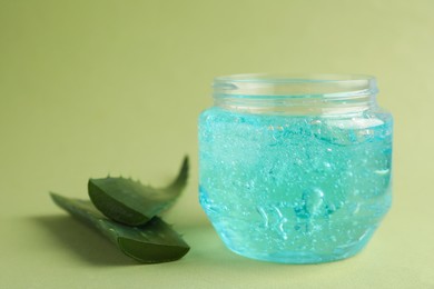 Jar of blue cosmetic gel and aloe on green background