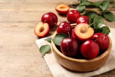 Photo of Delicious ripe cherry plums with leaves on wooden table. Space for text