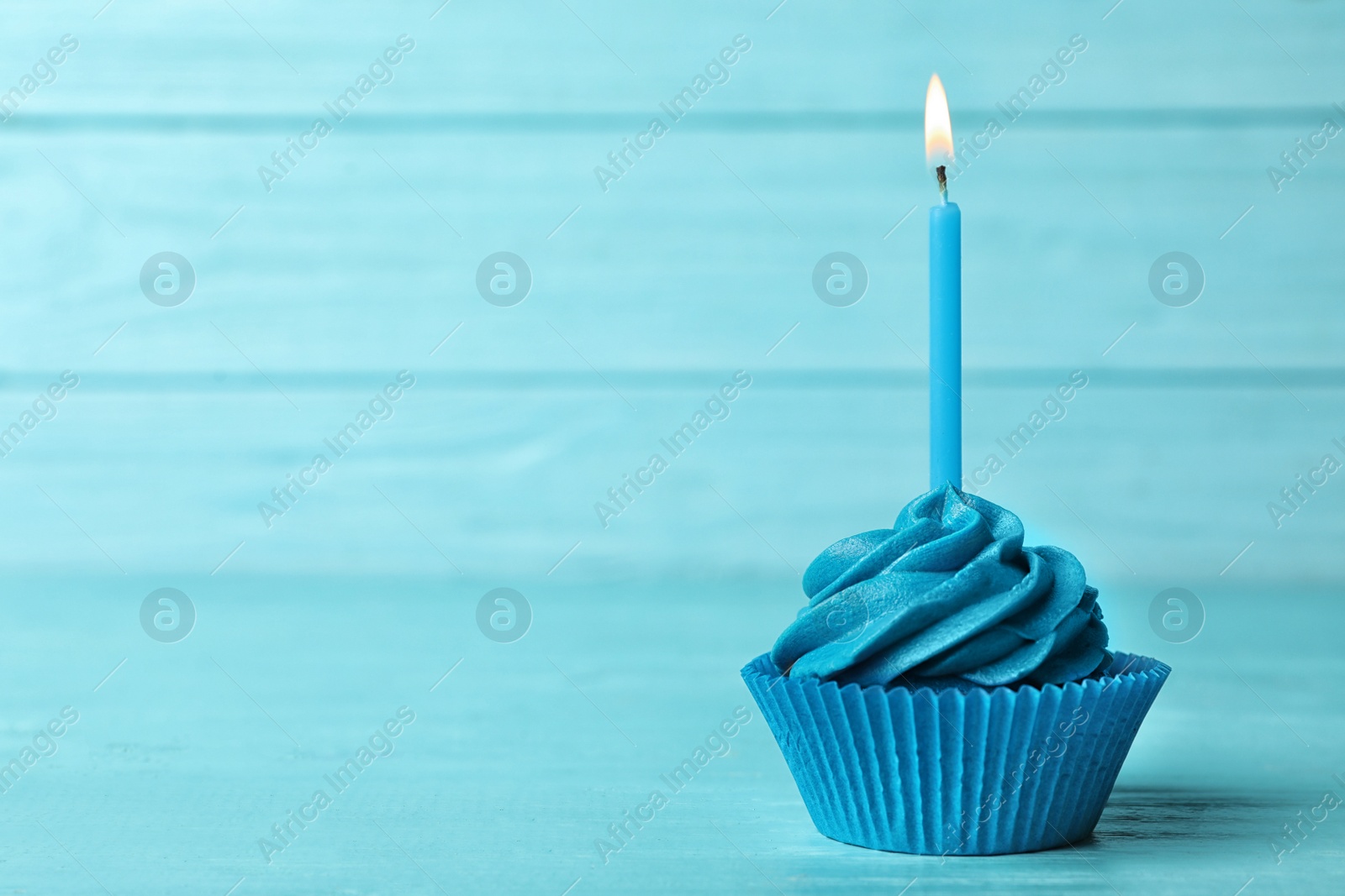 Photo of Delicious birthday cupcake with cream and burning candle on blue wooden background. Space for text