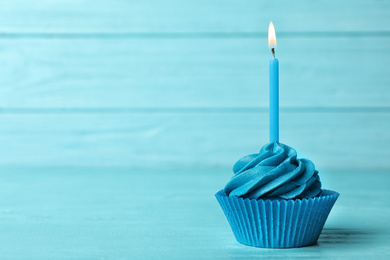 Delicious birthday cupcake with cream and burning candle on blue wooden background. Space for text