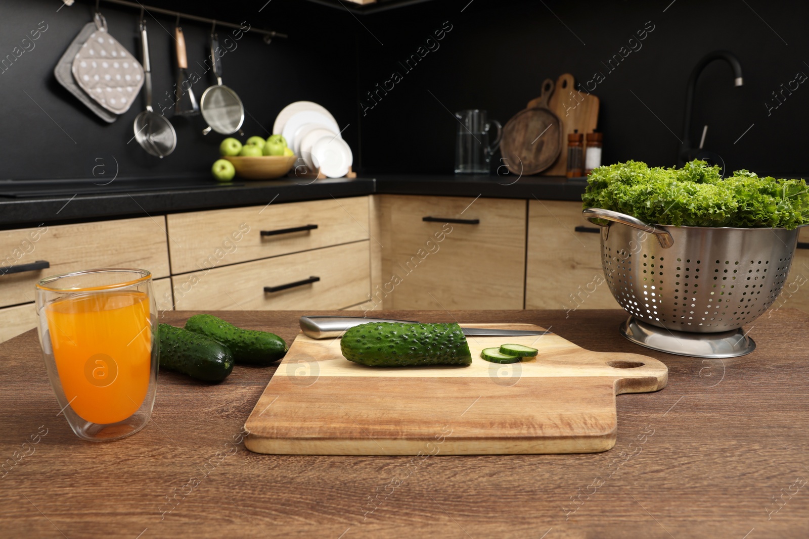 Photo of Cucumbers, lettuce and glass of juice on wooden table in kitchen