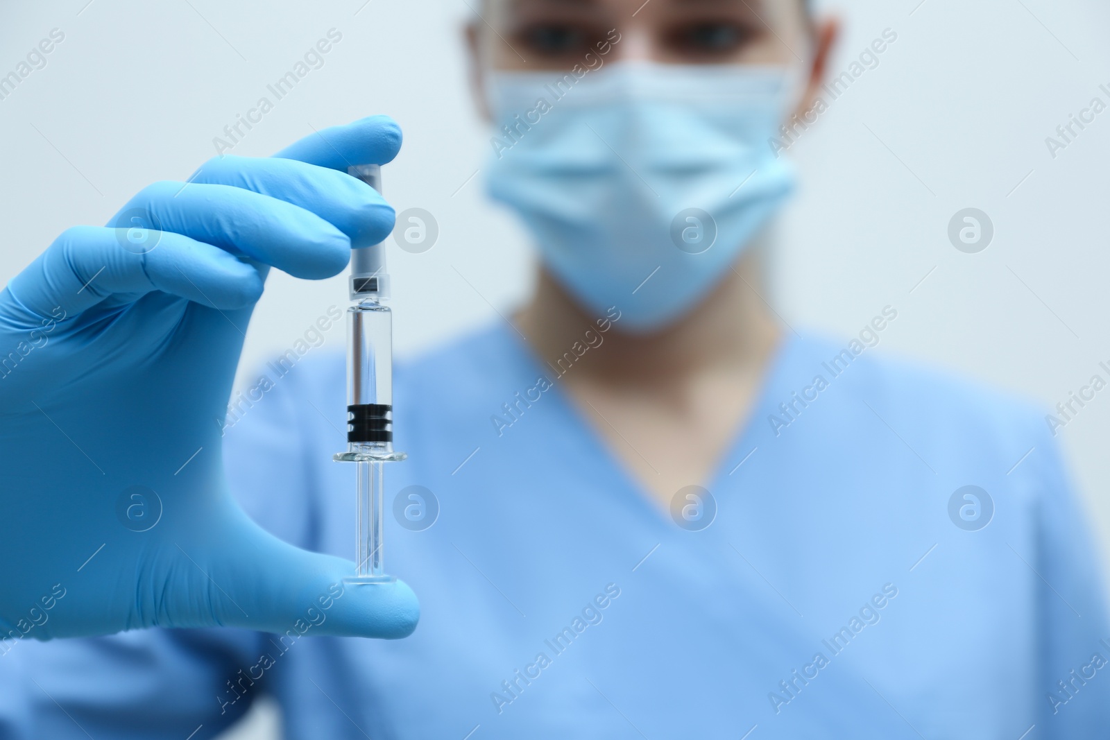 Photo of Doctor holding syringe with COVID-19 vaccine on light background, closeup