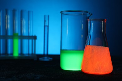 Laboratory glassware with luminous liquids on table against light blue background, selective focus. Space for text