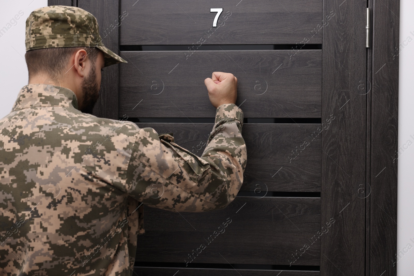 Photo of Military commissariat representative knocking on wooden door, back view