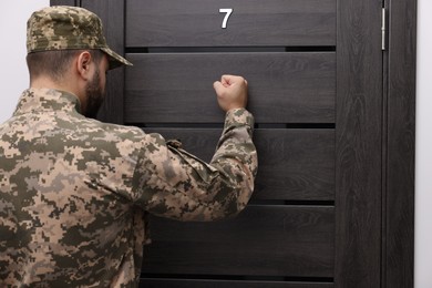 Photo of Military commissariat representative knocking on wooden door, back view