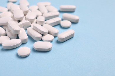 Photo of Many pills on light blue background, closeup. Space for text