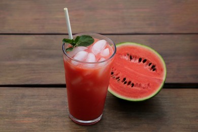 Photo of Glass of delicious watermelon drink with mint, ice cubes and fresh cut fruit on wooden table