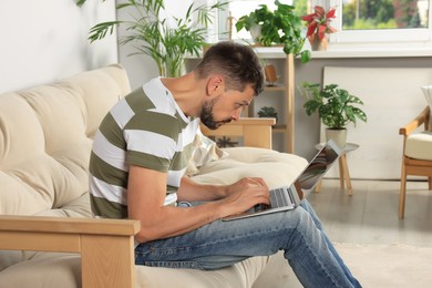 Photo of Man with poor posture using laptop on sofa at home