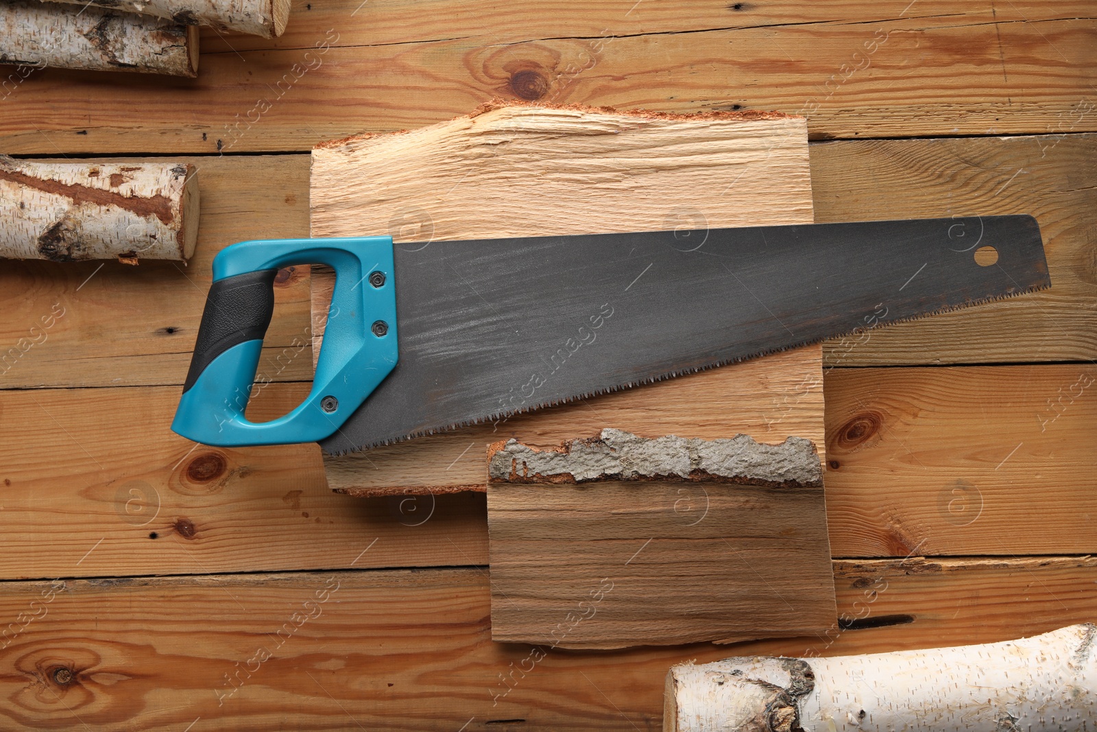 Photo of Saw with light blue handle and logs on wooden background, flat lay
